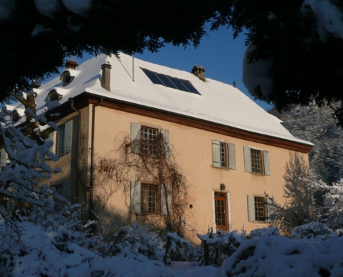 Ferme du Geissberg à Biederthal en hiver : maison enneigée entourée d'arbres dépouillés sous un ciel bleu dégagé, au cœur d'un environnement naturel préservé.