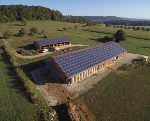 Vue aérienne en haute définition de la ferme du Geissberg à Biederthal, avec ses bâtiments agricoles équipés de grands panneaux solaires en toiture, au cœur de la campagne alsacienne.